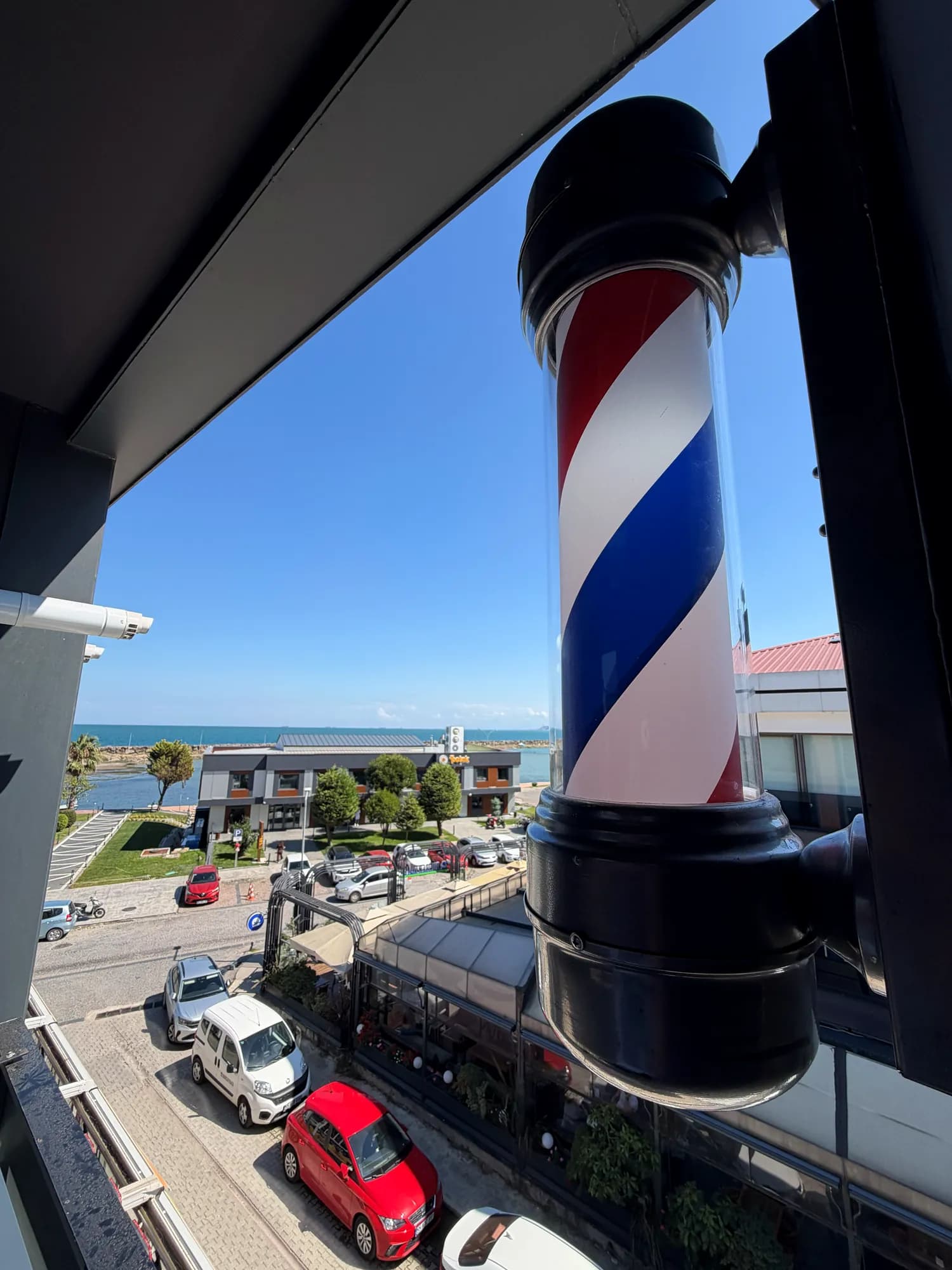 Rain Barber Studio'nun cephesindeki klasik barber direği; arkasında Körfez Vista Marina ve Karadeniz