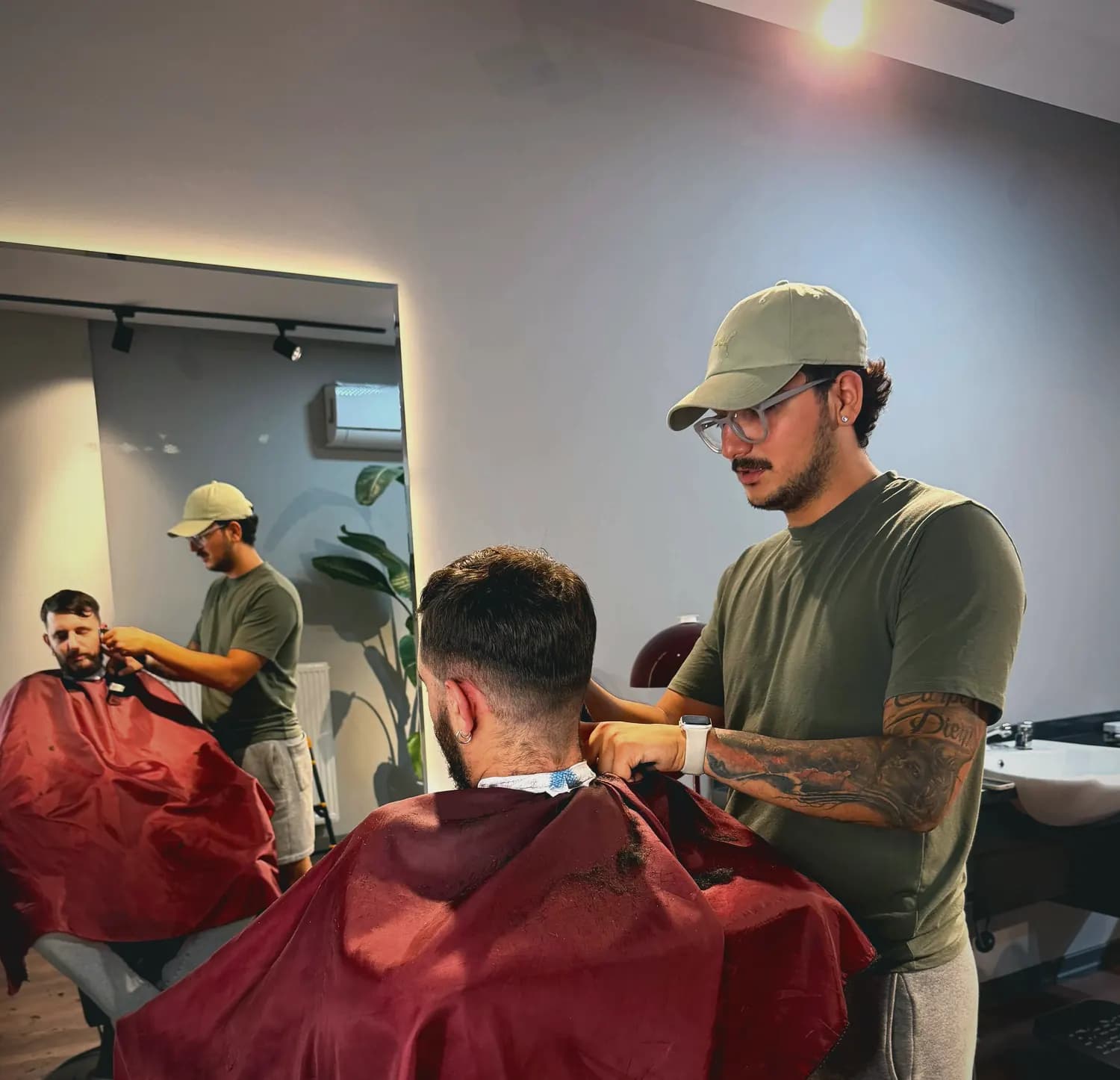 Berber, müşterinin ense hattını makineyle alırken; arkada ayna yansıması