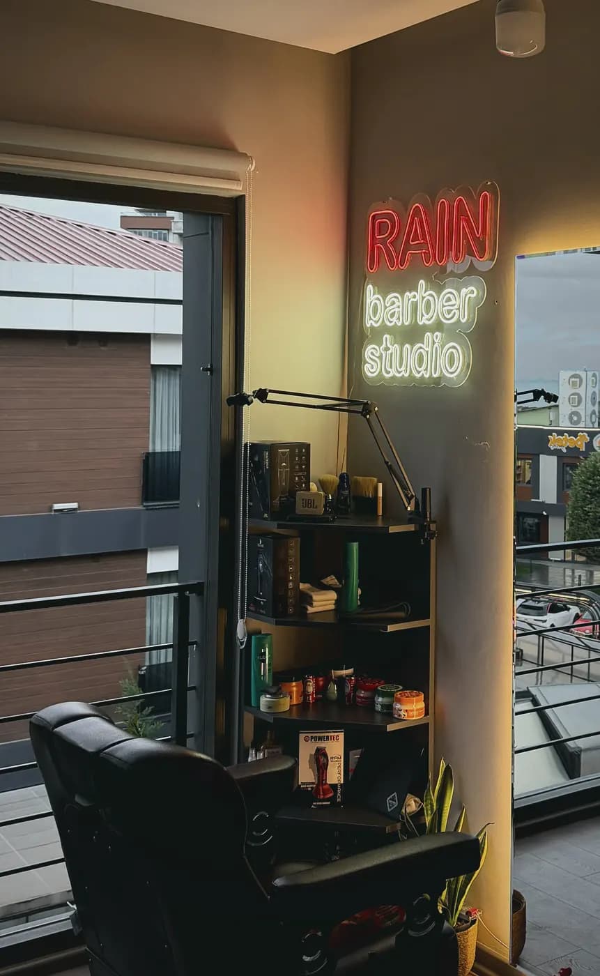 Stüdyo duvarındaki Rain Barber Studio neon tabelası ve ürün rafı